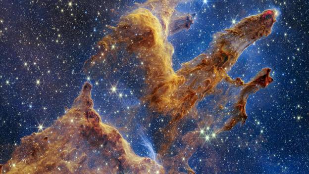 “Pillars of Creation” captured in NASA’s James Webb Space Telescope’s near-infrared view. The pillars resemble arches and spires rising from a desert, but are filled with semitransparent gas and dust.